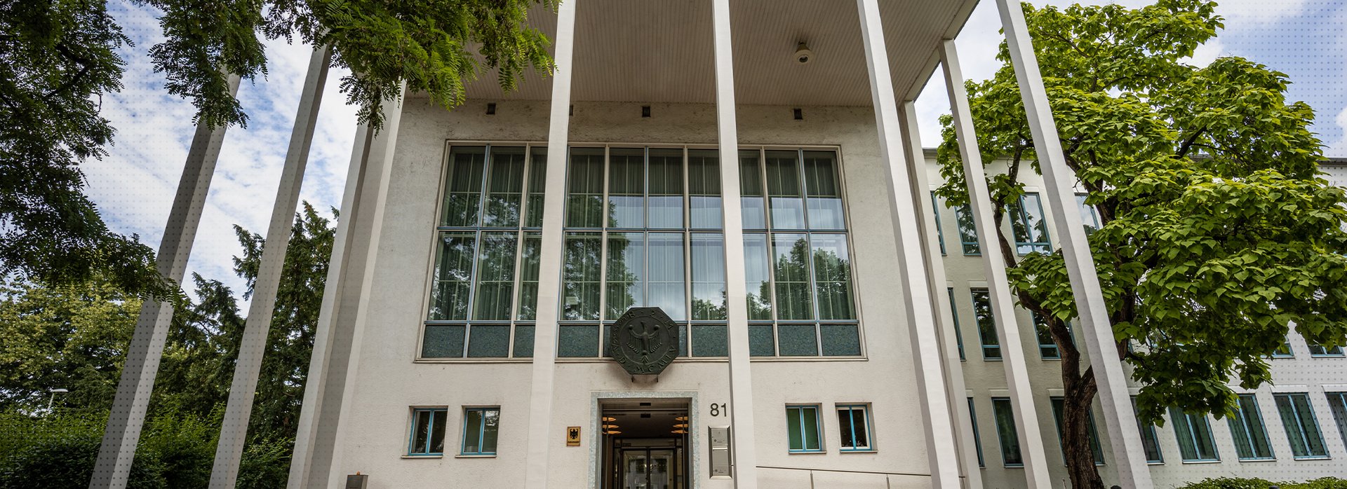 Das Foto zeigt den Haupteingang des Bundesrechnungshofes in Bonn in der Abendd&auml;mmerung. Im Vordergrund sind Stra&szlig;enlaternen erleuchtet.