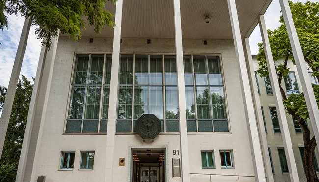 Das Foto zeigt den Haupteingang des Bundesrechnungshofes in Bonn in der Abendd&auml;mmerung. Im Vordergrund sind Stra&szlig;enlaternen erleuchtet.