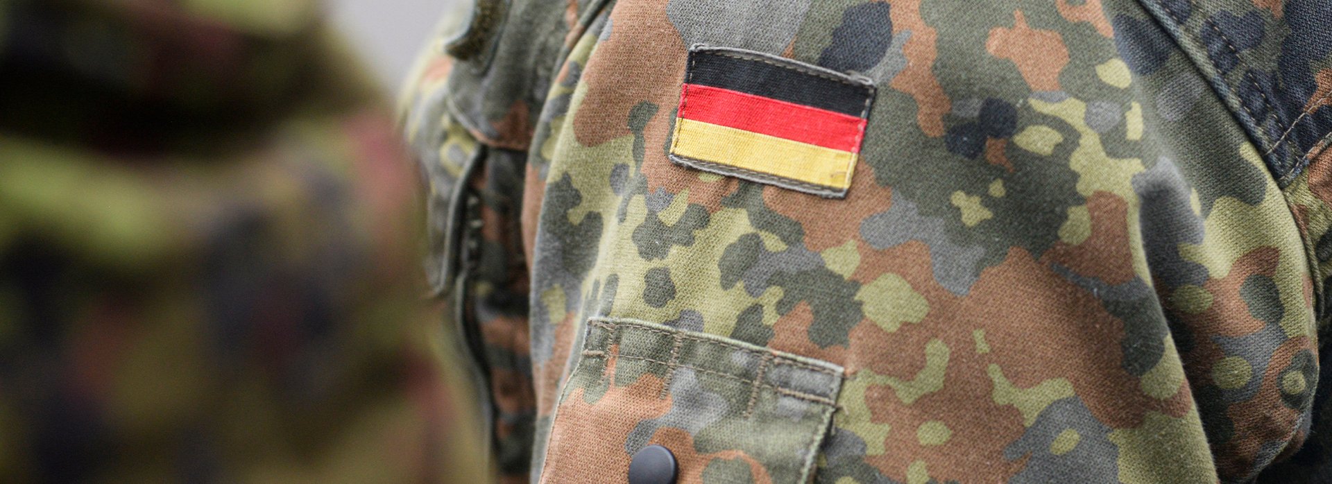 Ausschnitt des Feldanzugs eines Bundeswehrsoldaten mit Fokus auf die Deutschlandfahne auf dem Oberarm.