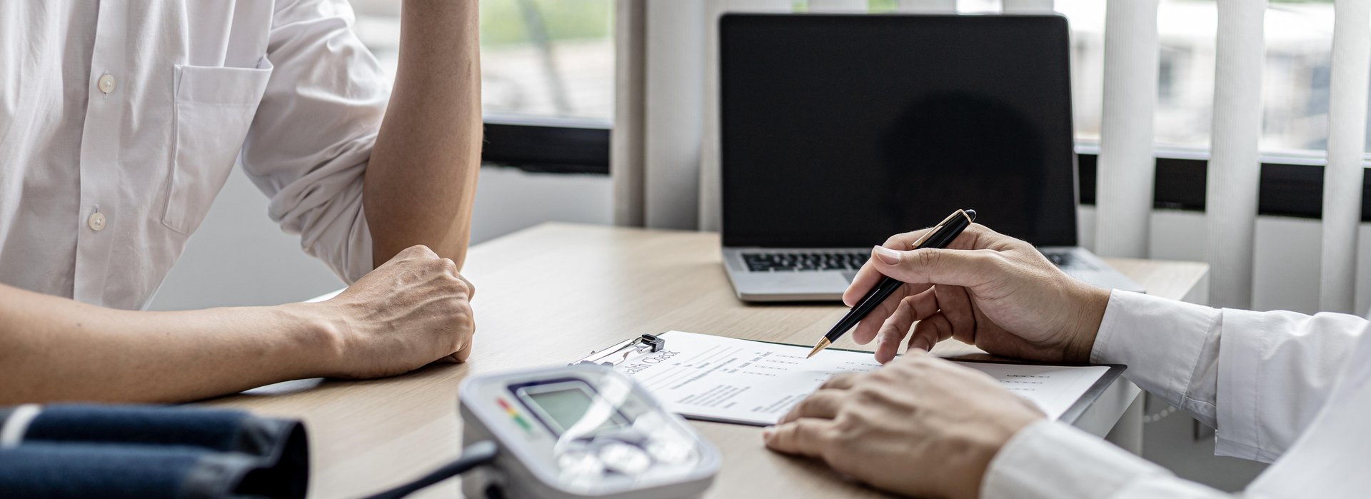 Ein Patient sitzt mit einem Arzt am Tisch. Der Arzt spricht mit dem Patienten anhand einer Checkliste.
