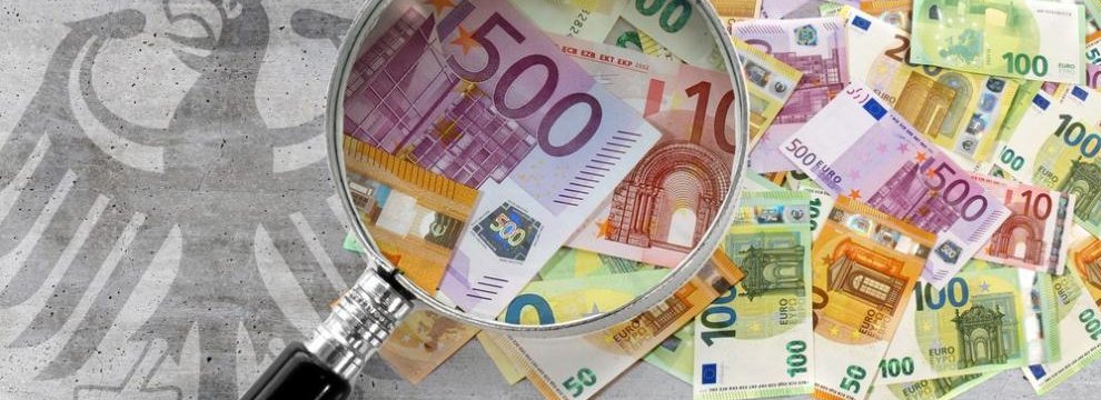 Das Foto zeigt einen losen Haufen an verschiedenen Euro-Geldscheinen. Eine Lupe vergr&ouml;&szlig;ert einige Scheine. Neben den Geldscheinen ist der Bundesadler auf grauen Beton gemalt. Montage: Bundesrechnungshof
