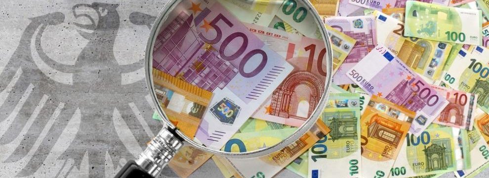 Das Foto zeigt einen losen Haufen an verschiedenen Euro-Geldscheinen. Eine Lupe vergr&ouml;&szlig;ert einige Scheine. Neben den Geldscheinen ist der Bundesadler auf grauen Beton gemalt. Montage: Bundesrechnungshof