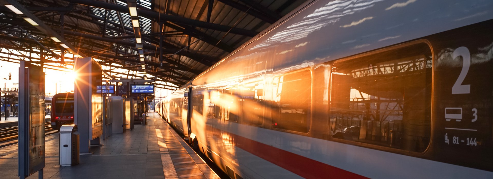 Ein ICE steht am menschenleeren, &uuml;berdachten Bahnsteig. Auf dem gegen&uuml;berliegenden Gleis f&auml;hrt ein Regionalzug in den Sonnenuntergang.