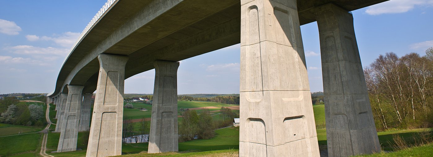 Das Bild zeigt eine lange Straßenbrücke, die über eine grüne Landschaft führt.