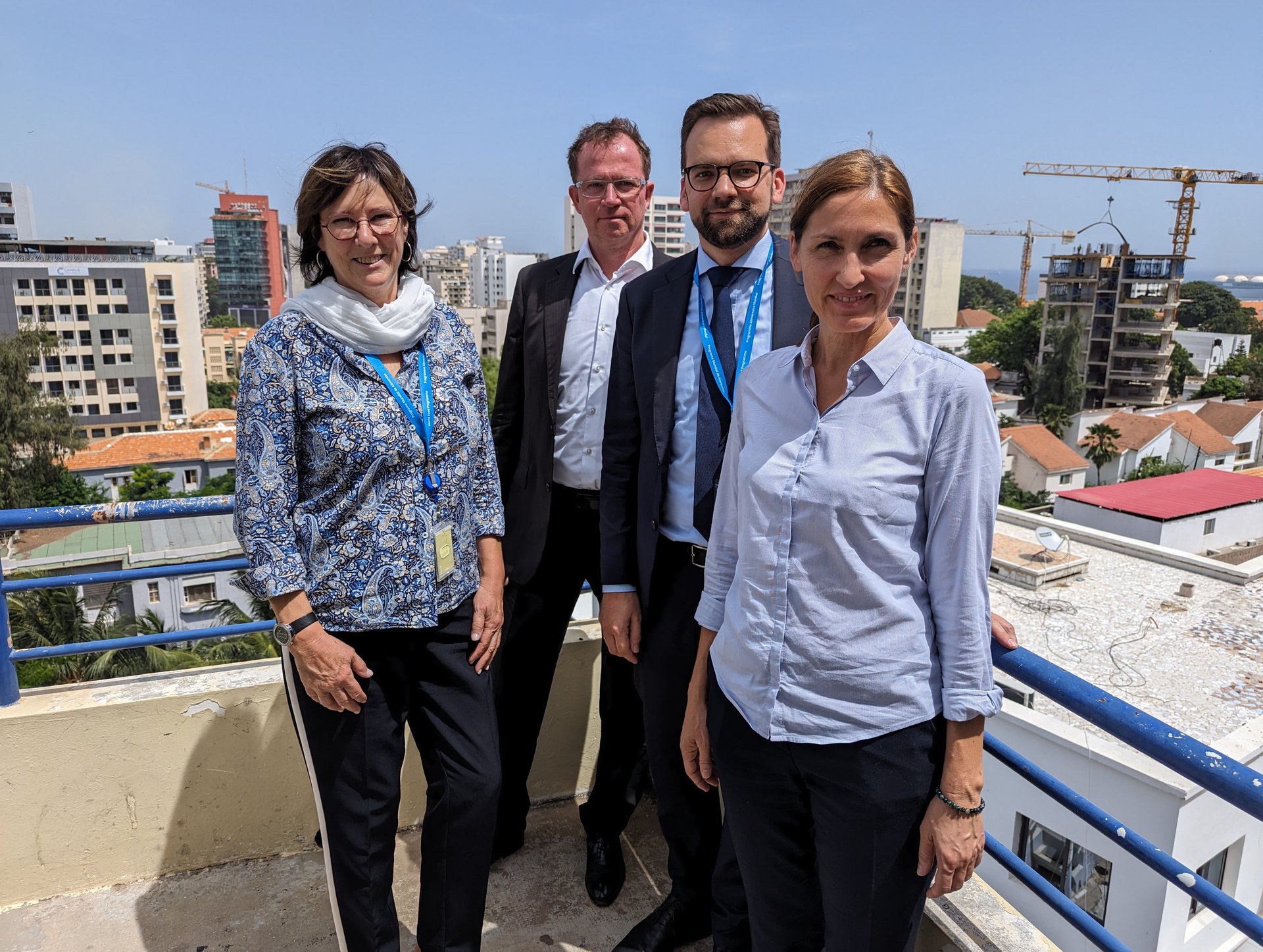Das Foto zeigt vier Personen, die auf der Dachterrasse eines Hauses stehen. Im Hintergrund sind Hochh&auml;user und Baukr&auml;ne vor einem blauen Himmel zu sehen.