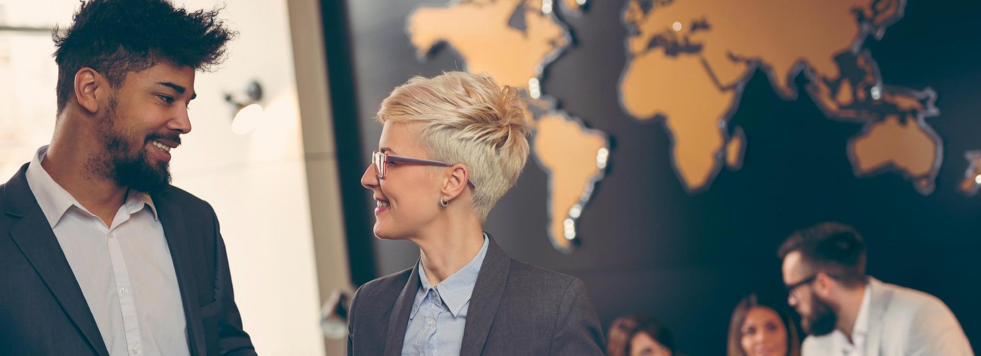Two people are talking. There is a map of the world in the background.