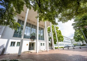 Das Foto zeigt den Haupteingang des Bundesrechnungshofes in Bonn, Adenauerallee 81. Im Hintergrund ist der vordere Geb&auml;udefl&uuml;gel sowie ein gl&auml;serner &Uuml;bergang zu sehen.
