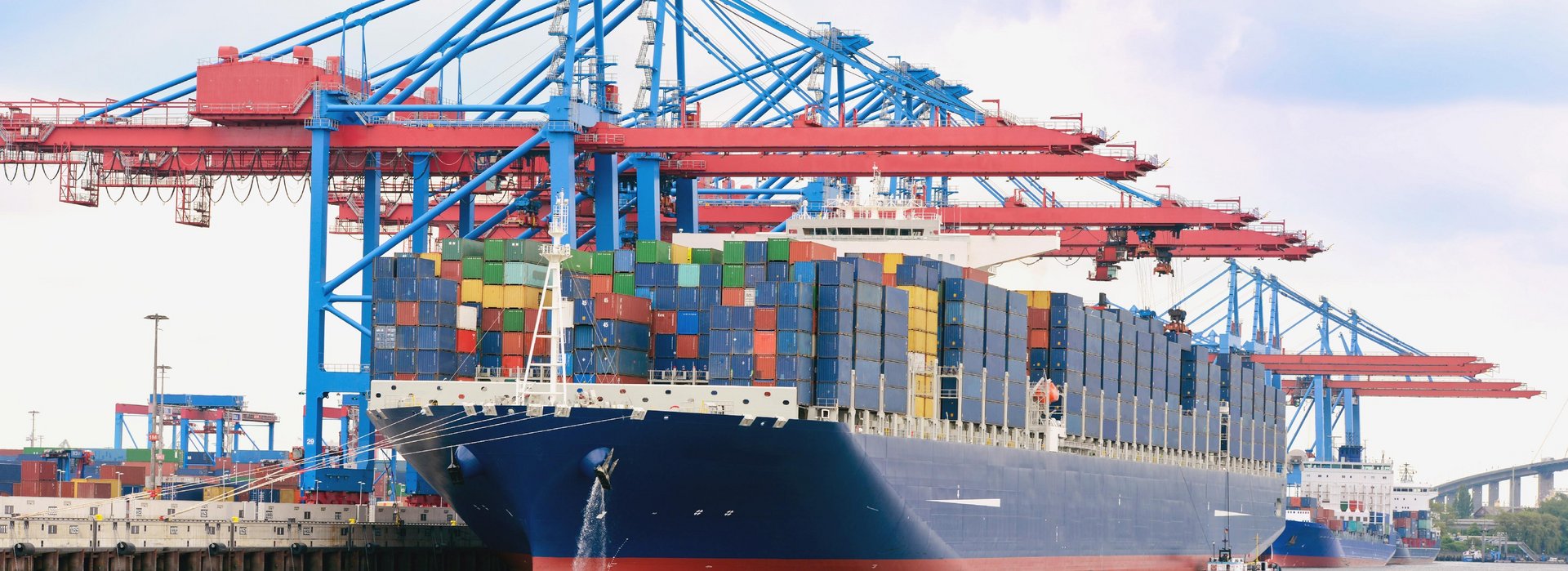 A fully loaded container ship in a harbor. Above the boat you can see various cranes for loading the ship.